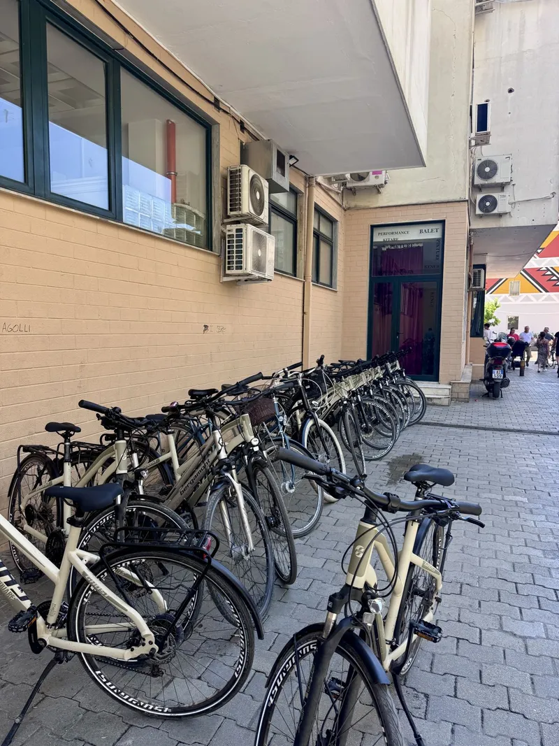 A long row of beige rental bicycles parked along the wall of the BikeTirana shop