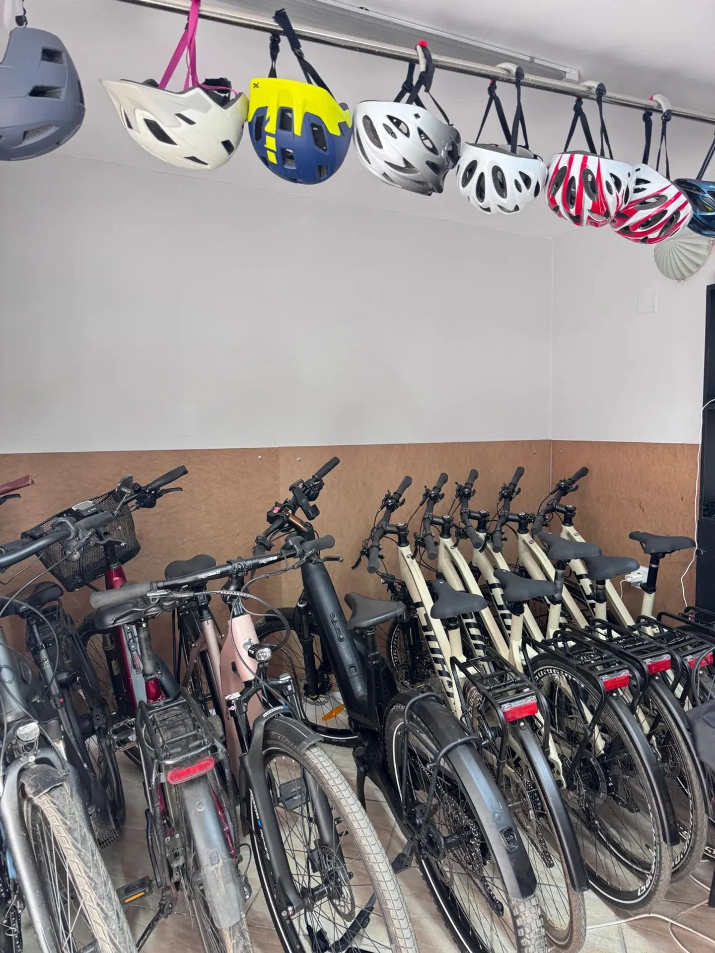 A row of parked bicycles with colorful helmets hanging on a rack above them in the workshop