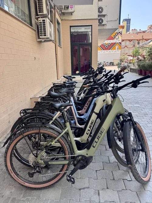 En række olivengrønne og sorte Cube-elcykler parkeret i en brolagt gyde